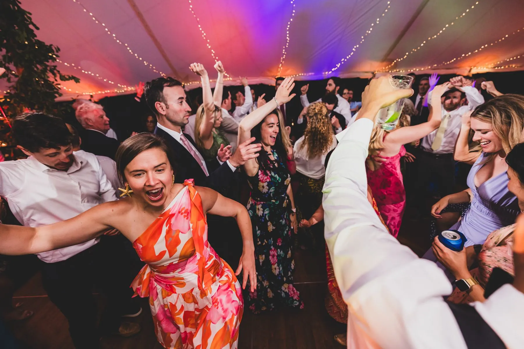 Guests dancing in summer dresses under the tent lights